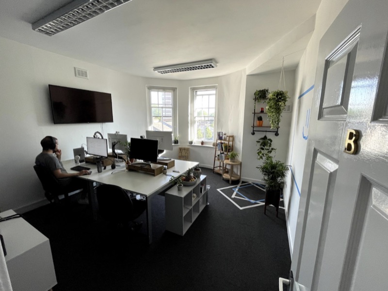 incident.io's first London office: desks, a TV and plants by two tall windows